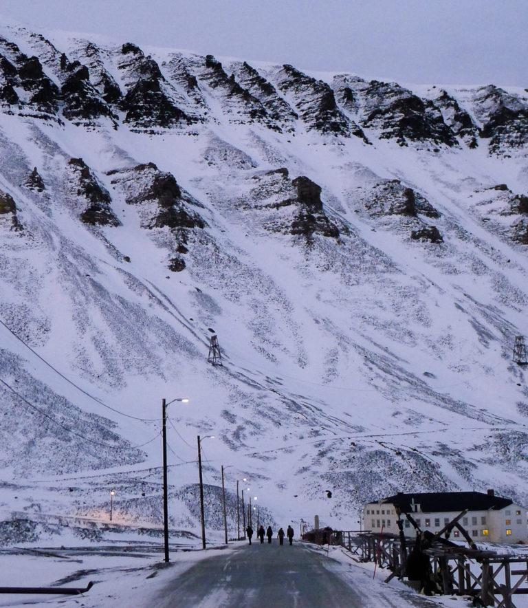 The mighty cliff edge that hangs over Longyearbyen with old relics of its bygone mining era like patchwork on the slopes © William Copeland